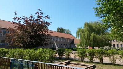 Bild vergr&ouml;&szlig;ern: Von der Straße aus blickt man über das begrünte Schulgelände auf das Schulgebäude.
