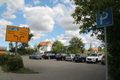 Kleiner Parkplatzam Rosengarten mit parkenden Autos. Im Hintergrund sind Schloß und Stiftskirche zu sehen.