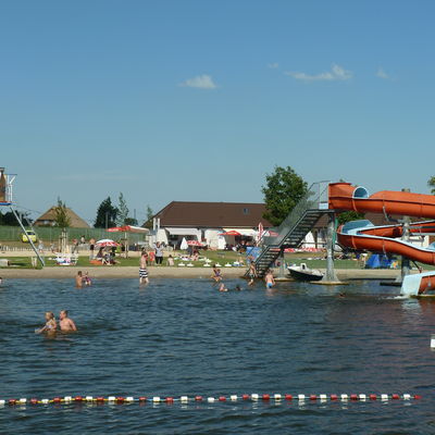 Von der Wasserseite aus fällt der Blick auf das Gelände des Freibades. Zu sehen sind unter anderem Wasserrutsche, Liegewiese und Spielplatz.